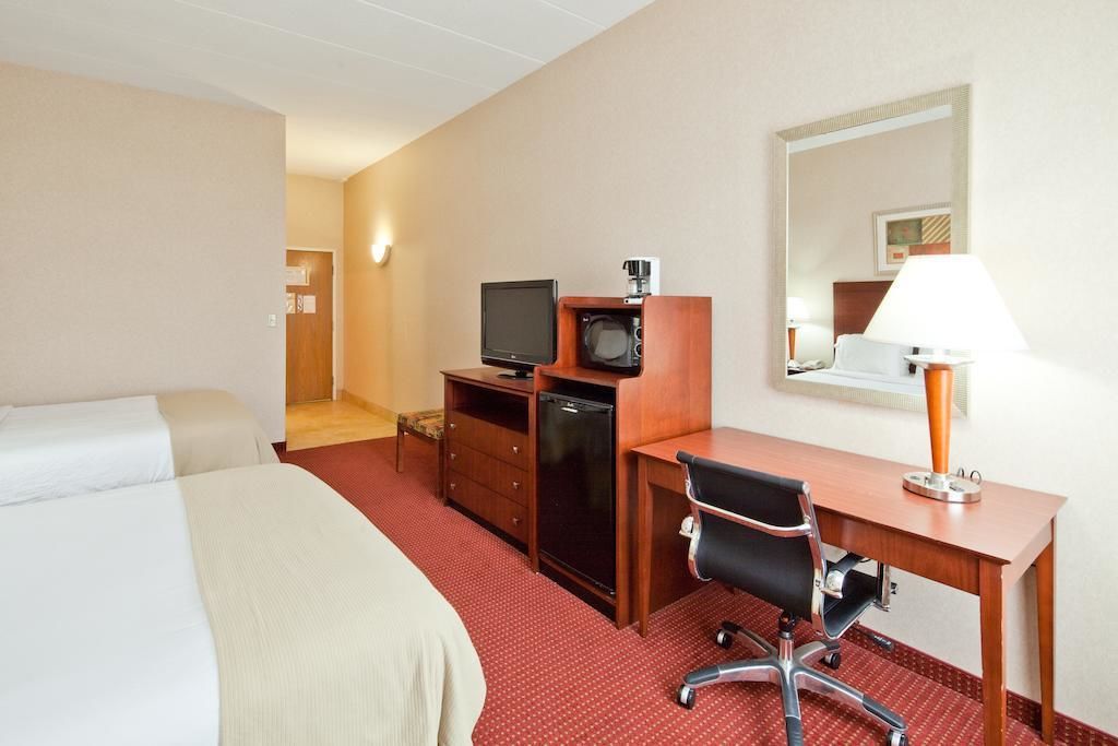 A hotel room with a bed, a desk with a computer, a television, and a lamp.
