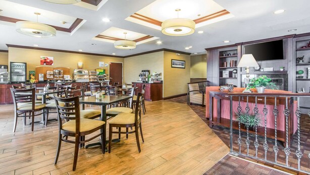 Un comedor amplio con mesas y sillas de madera, una zona de bar central con un banco tapizado de rojo, y una cocina al fondo.