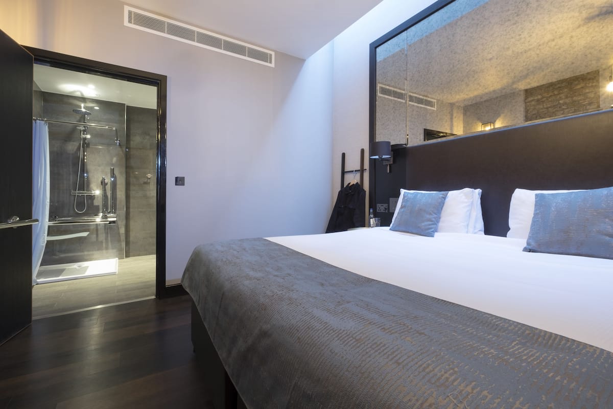 Moderni hotellihuone, jossa on suuri sänky, erillinen suihkutila ja suuri peili, joka heijastaa huonetta.