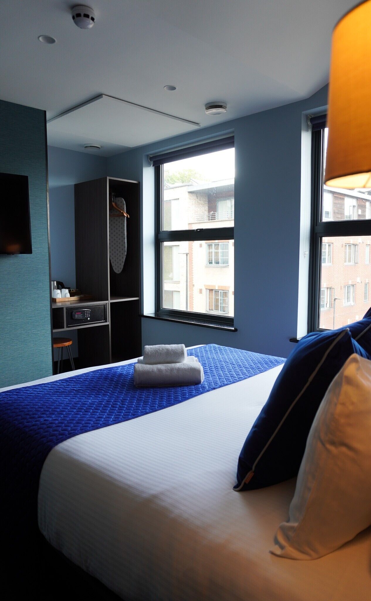 Habitación de hotel con cama, escritorio, armario y ventana con vista a edificios.