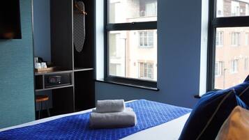 Ein Hotelzimmer mit Bett, Schreibtisch, Kleiderschrank und einem Fenster mit Blick auf Gebäude.