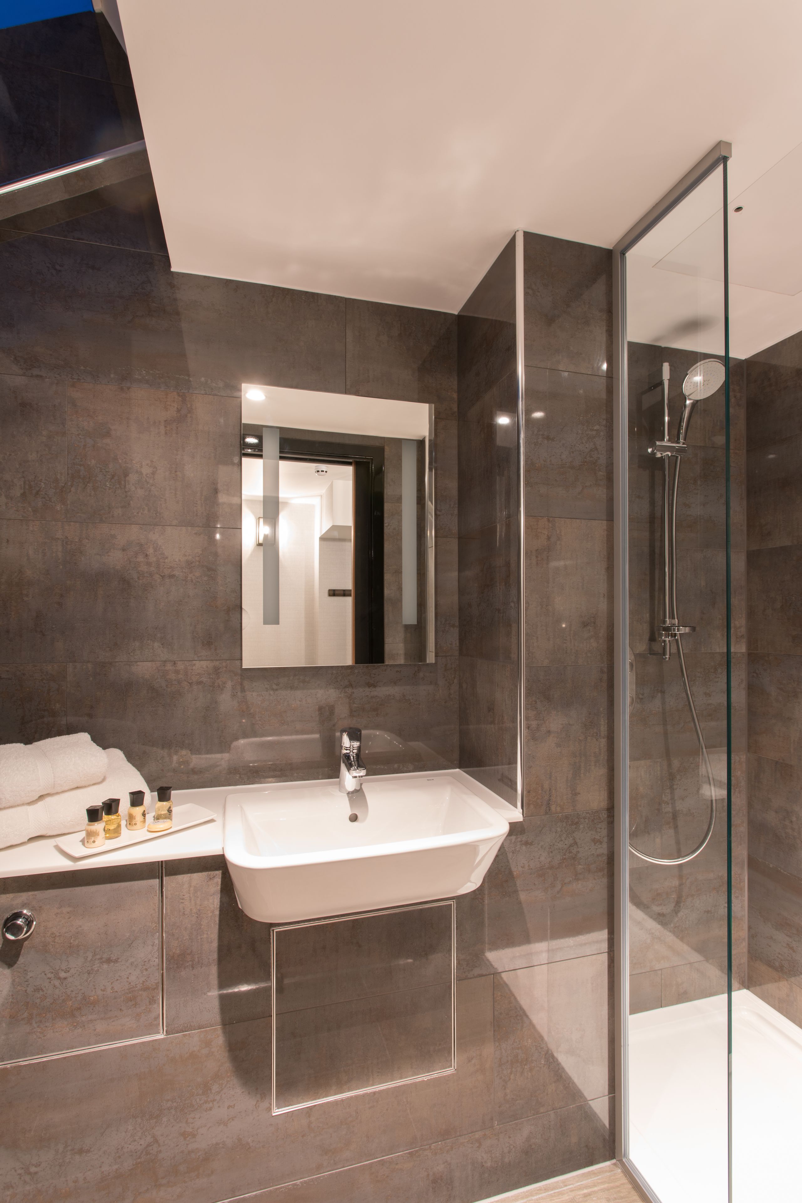Un bany modern amb dutxa de vidre, un mirall gran i un lavabo amb sabó i altres productes de higiene.