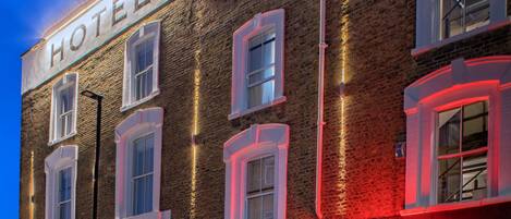 A hotel with a brick facade, illuminated signage, and a street view.