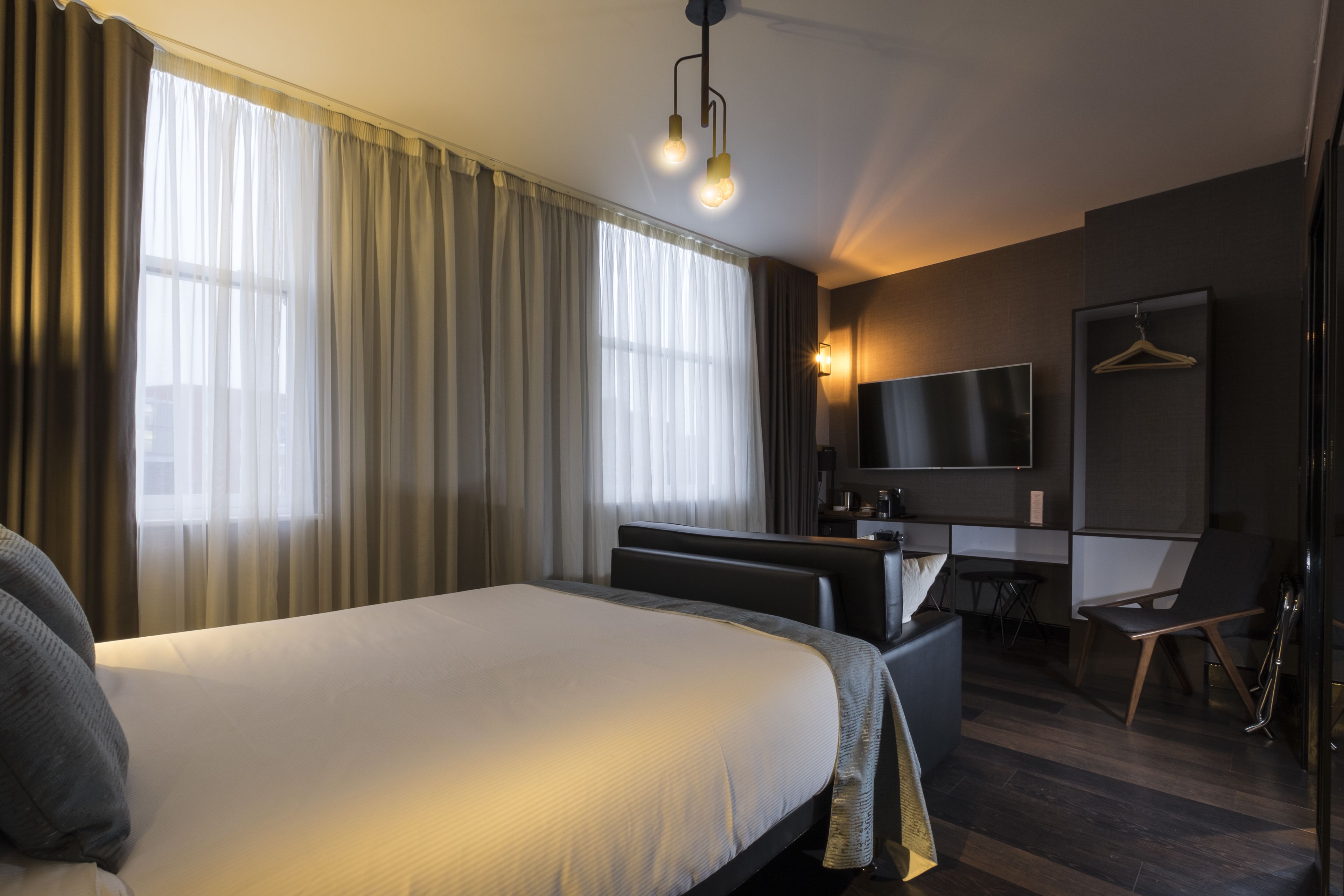A modern hotel room with a large bed, a desk, a chair, a TV, and a coat hanger.