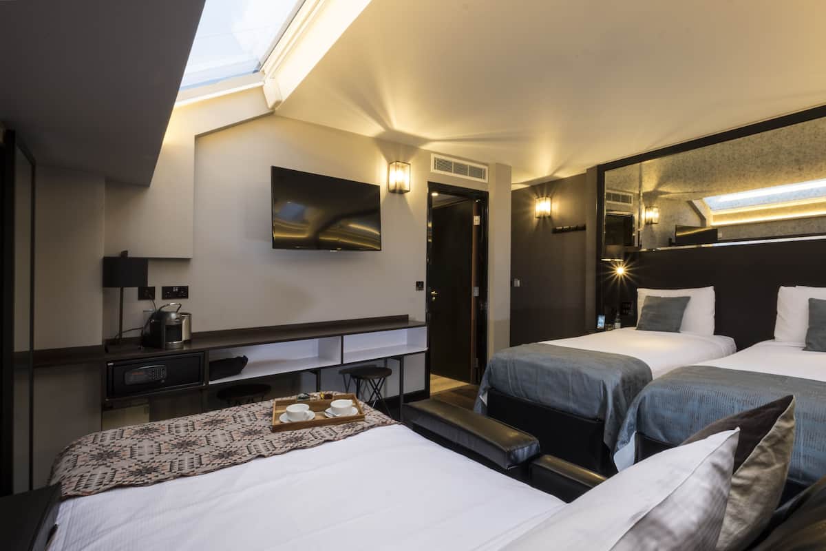 Hotellihuone, jossa on kaksi sänkyä, työpöytä, tuoli, pieni pöytä, jonka päällä on tarjoilualusta, sekä suuri peili.
