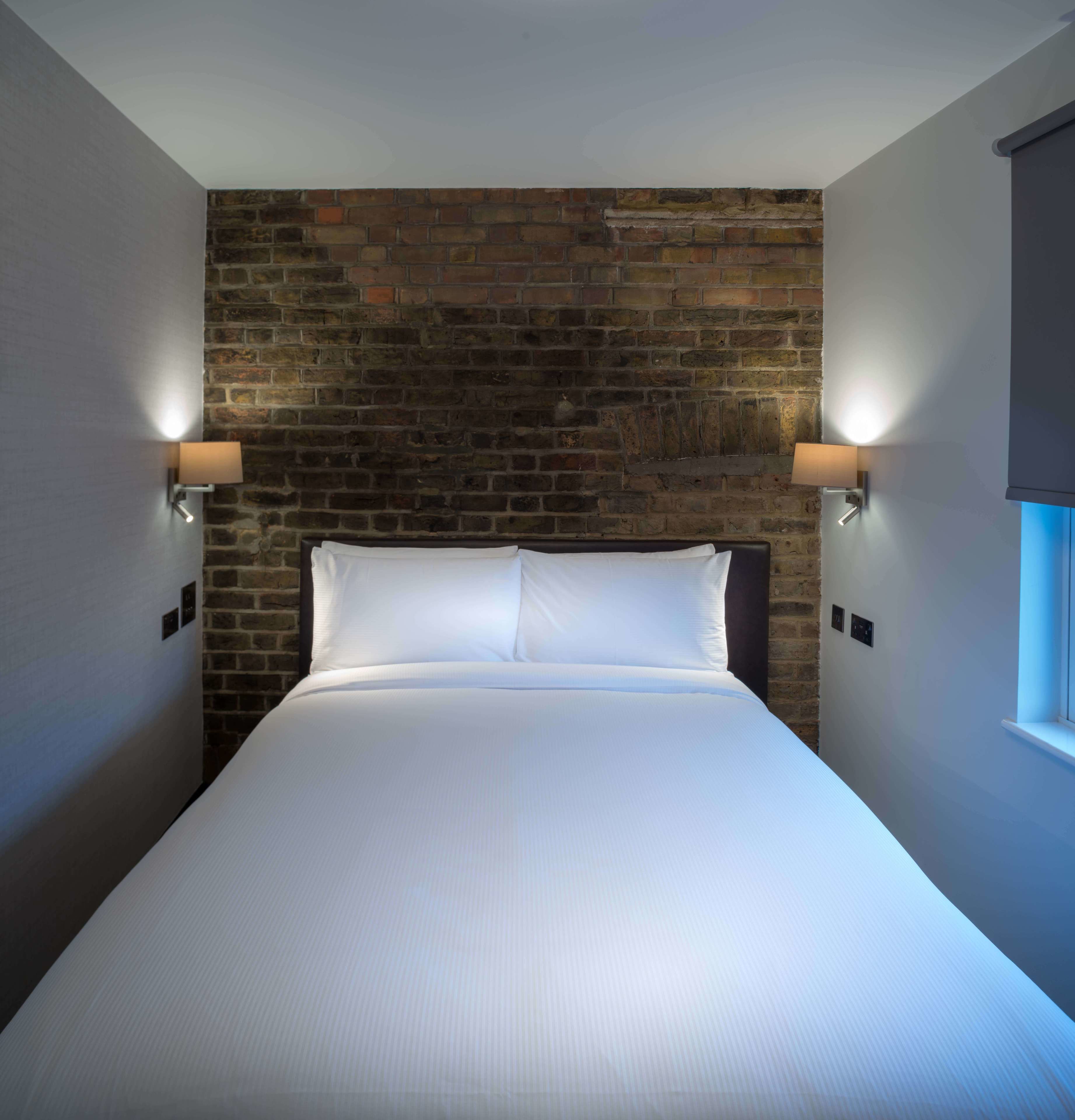 Ein Hotelzimmer mit Backsteinwand, einem großen Bett mit weißer Bettwäsche und zwei Wandlampen.
