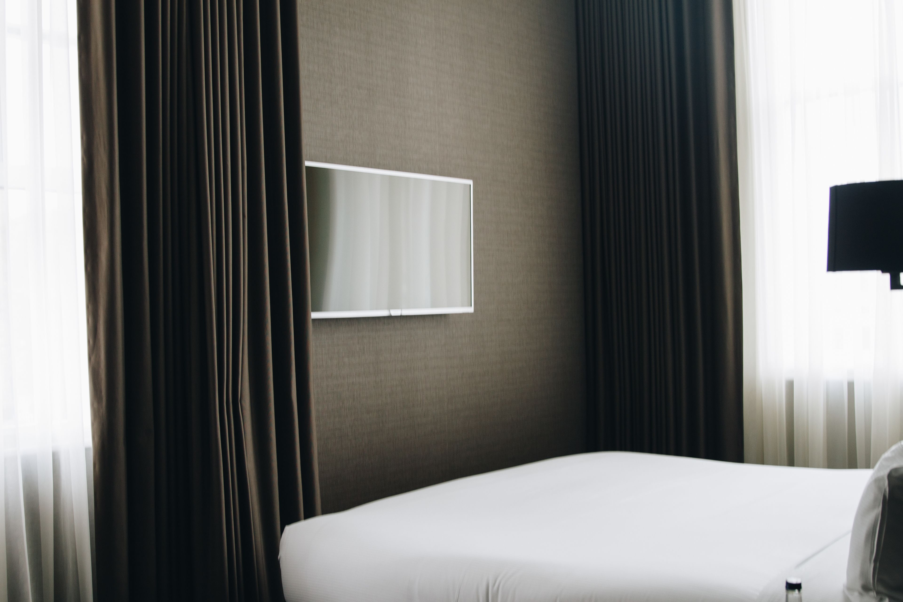 A hotel room with a bed, a flat-screen TV mounted on the wall, and a window with curtains.