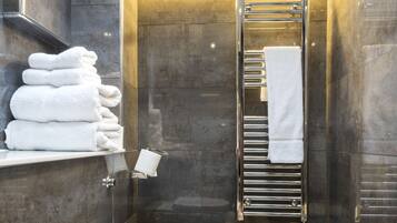 A modern bathroom with a stack of white towels, a glass shower enclosure, and a chrome towel rack.