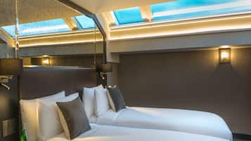 Habitació d'hotel moderna amb un llit gran, finestres de gresol i una taula petita amb gots i una ampolla.