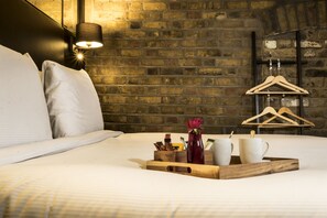 A neatly made bed with pillows, a tray with a vase and cups, and a brick wall with a hanging rack. - Camden Enterprise Hotel & Pub (London)