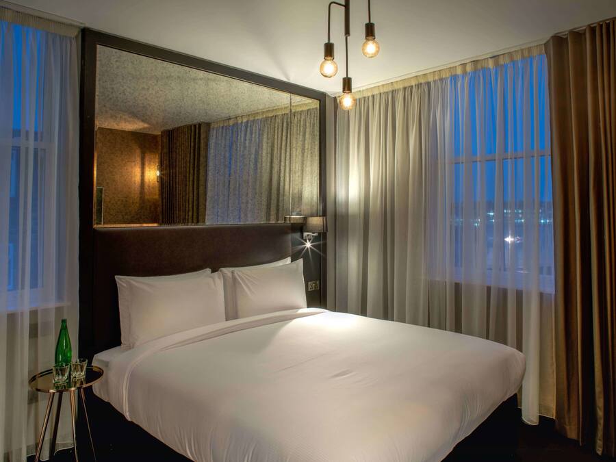 A large bed with a headboard, a bedside table with a lamp, and a mirror.