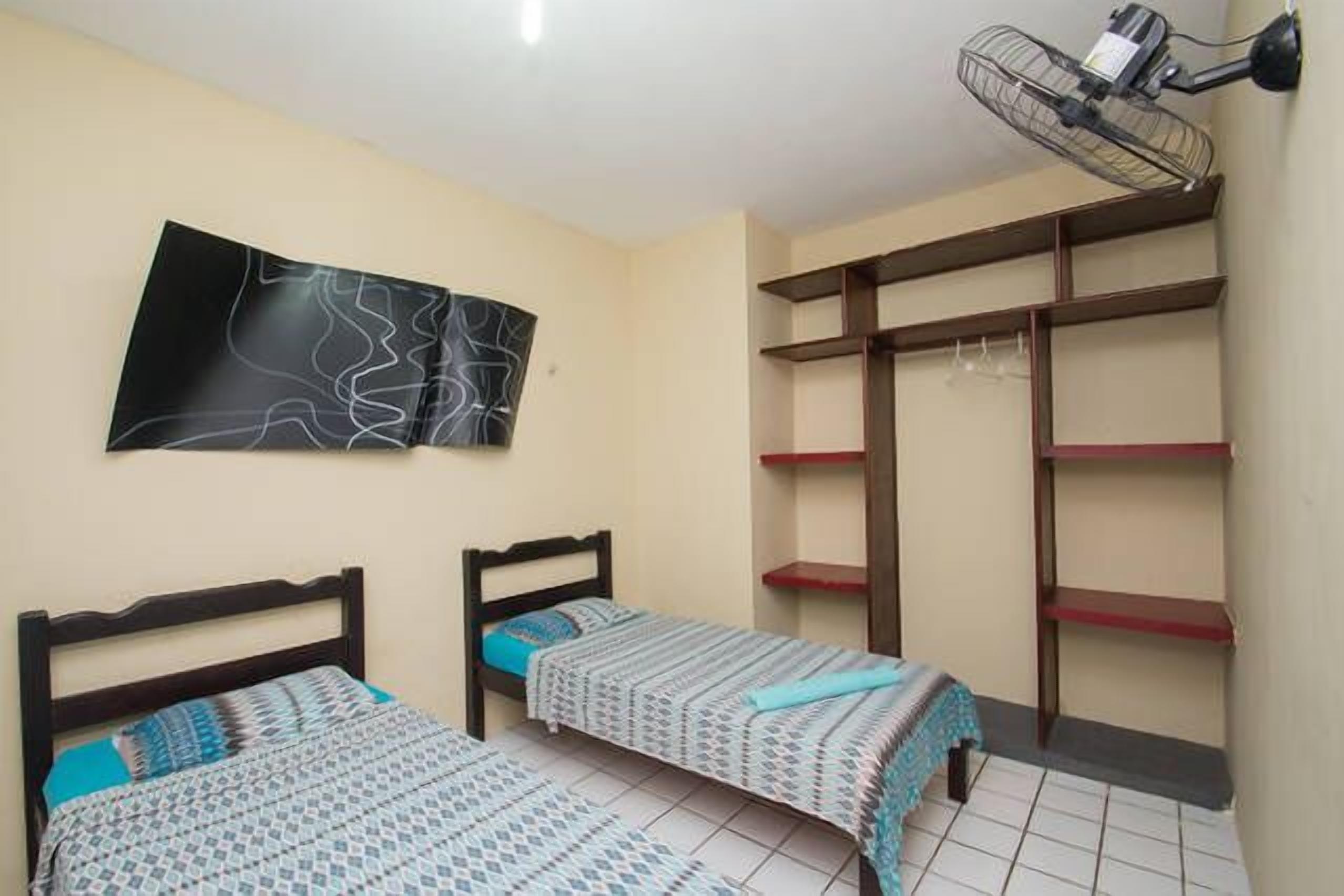 Une chambre avec deux lits, un ventilateur fixé au mur et un grand tableau abstrait.
