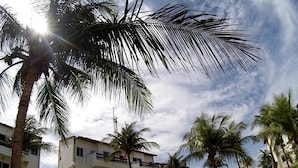 A multi-story building with balconies, surrounded by palm trees and a clear sky. - Apartamento Porto das Dunas - SBHS (Aquiraz)