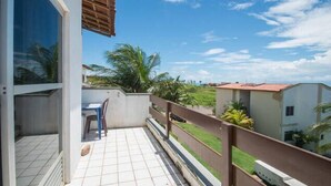 A balcony with a tiled floor, a chair, and a table. - Apartamento Porto das Dunas - SBHS (Aquiraz)