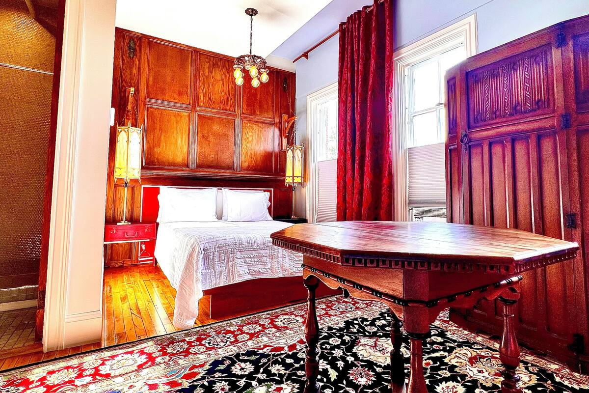 A traditional room with a wooden bed, a red curtain, and a patterned rug.