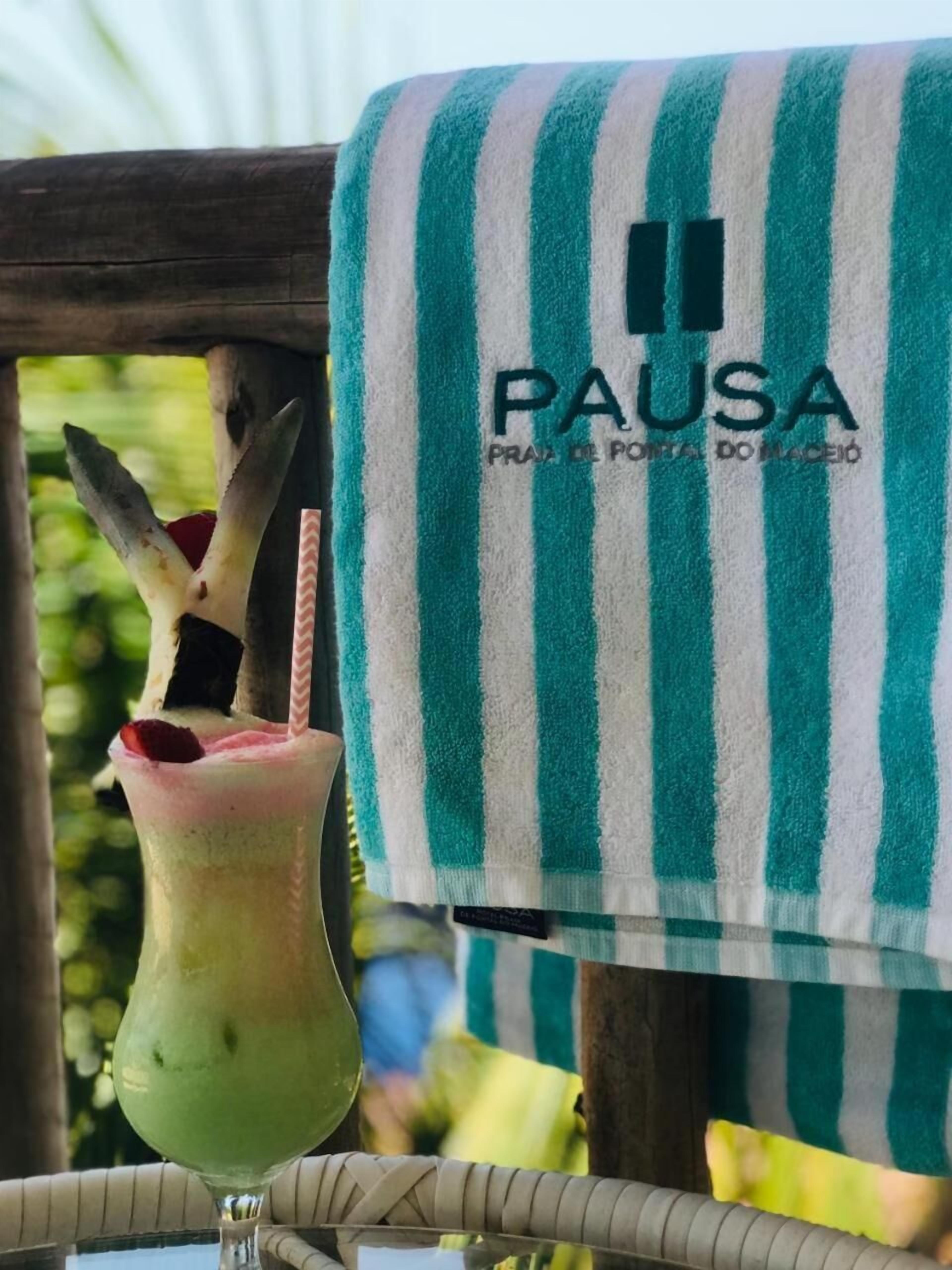 A green and white striped towel hanging on a wooden chair with a drink in a glass beside it.