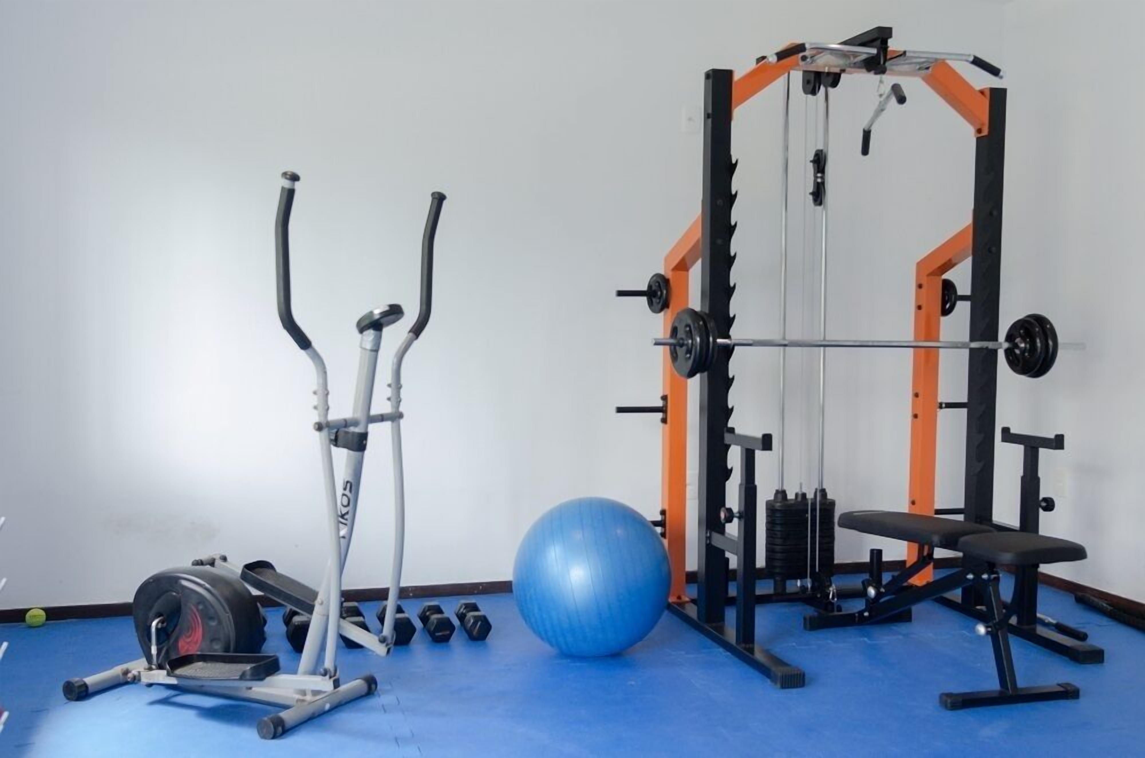 Uma academia com equipamentos de exercícios, incluindo um banco, halteres, uma bola medicinal e uma máquina de musculação.