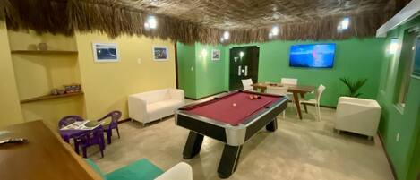 A room with a pool table, green walls, a TV, and a thatched ceiling.
