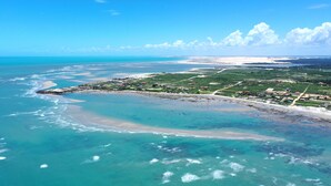An aerial view of a coastal area with a beach, clear waters, and a small settlement with houses and roads. - Pausa Hotel (Fortim)