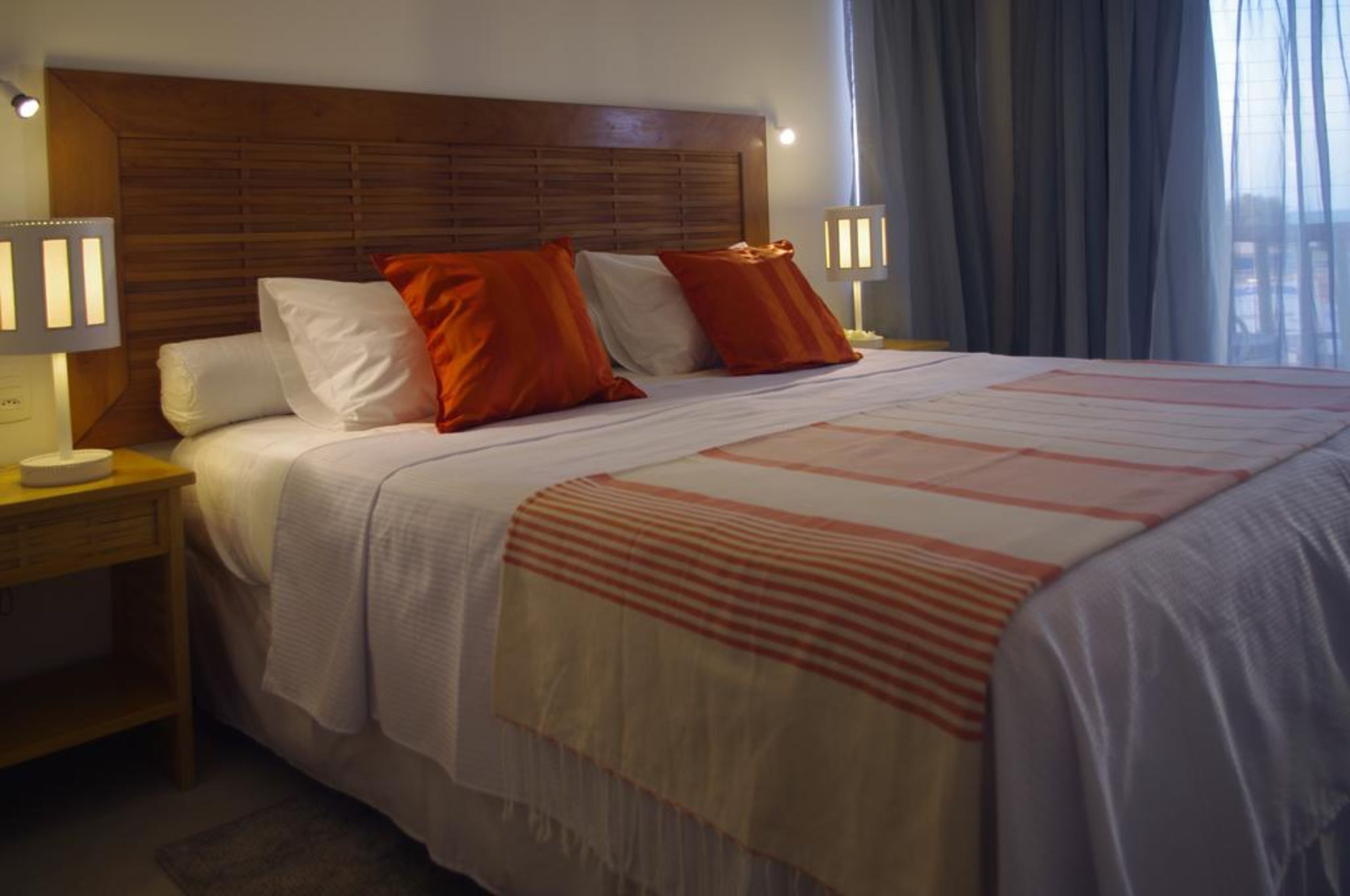 A neatly made bed with a striped blanket, two bedside lamps, and a wooden headboard.