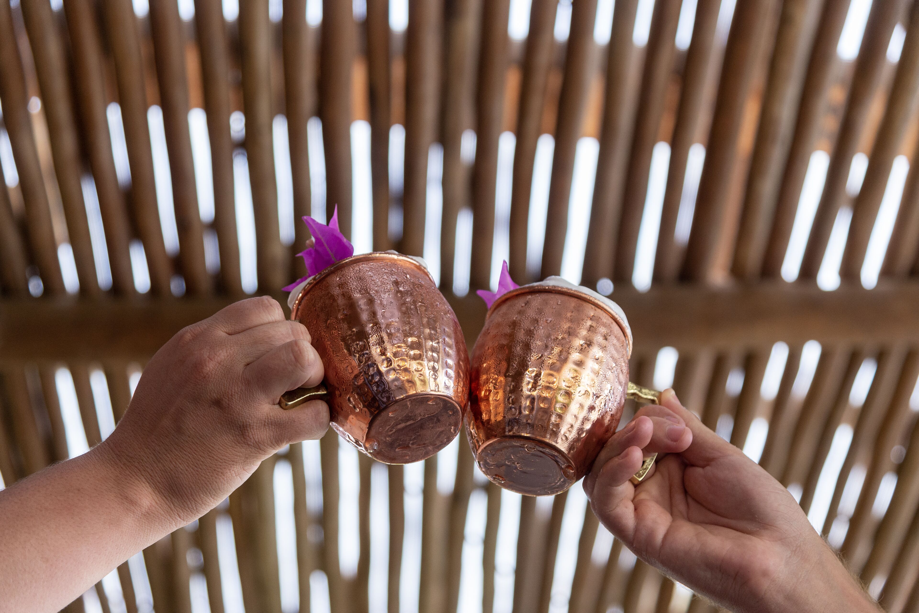 Two hands holding copper mugs with purple decorations.