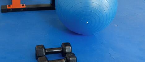 Een sportschool met trainingsapparatuur, waaronder gewichten, een blauwe trainingsbal en een rack voor squats.