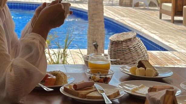 A dining table with breakfast items, a pool, and palm trees in the background. - Pausa Hotel (Fortim)