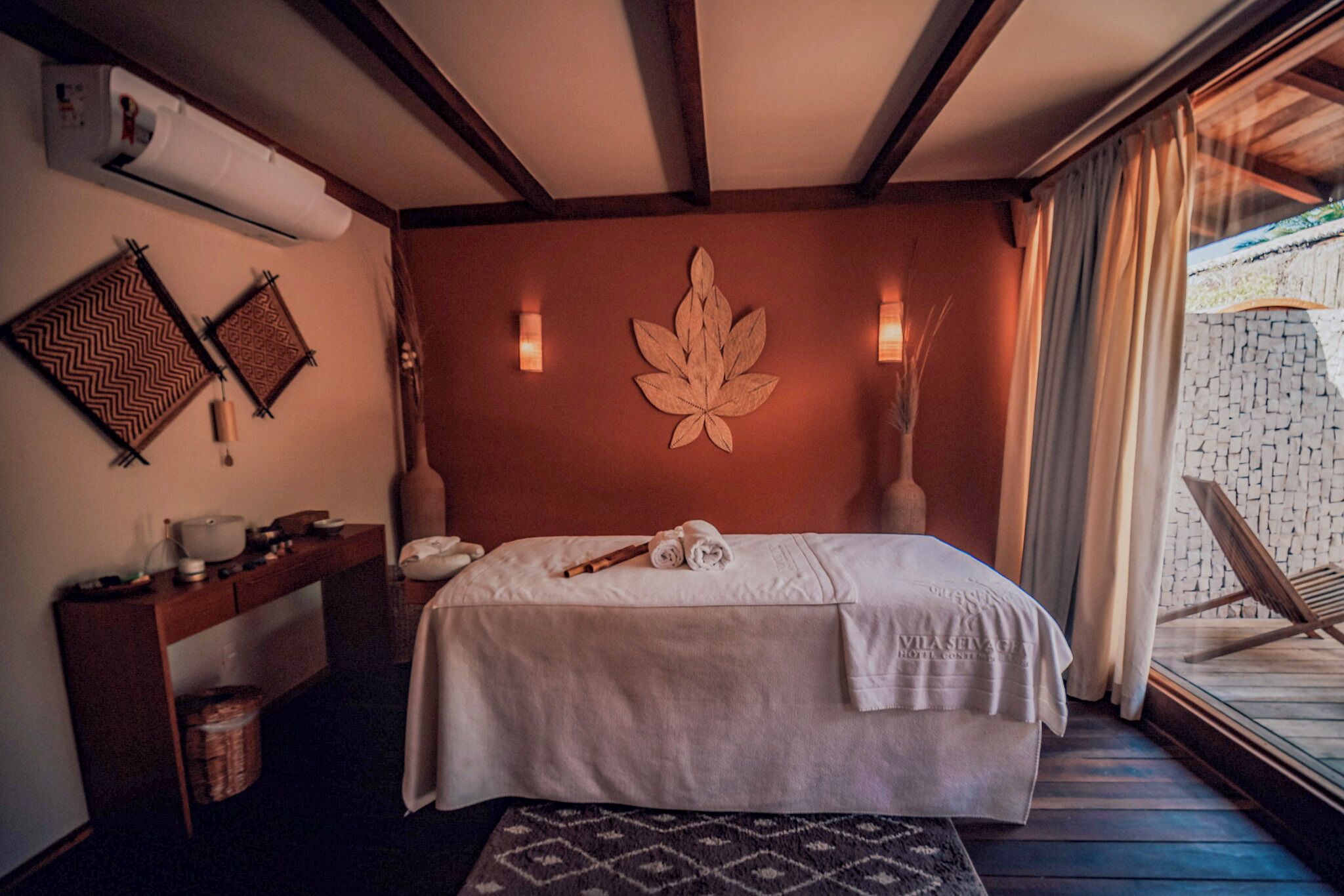 A bedroom with a bed, bedside table, wall decor, and a view of the outside.