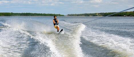 Uma pessoa praticando wakeboard em um corpo d'água, com céu claro e terra ao fundo.