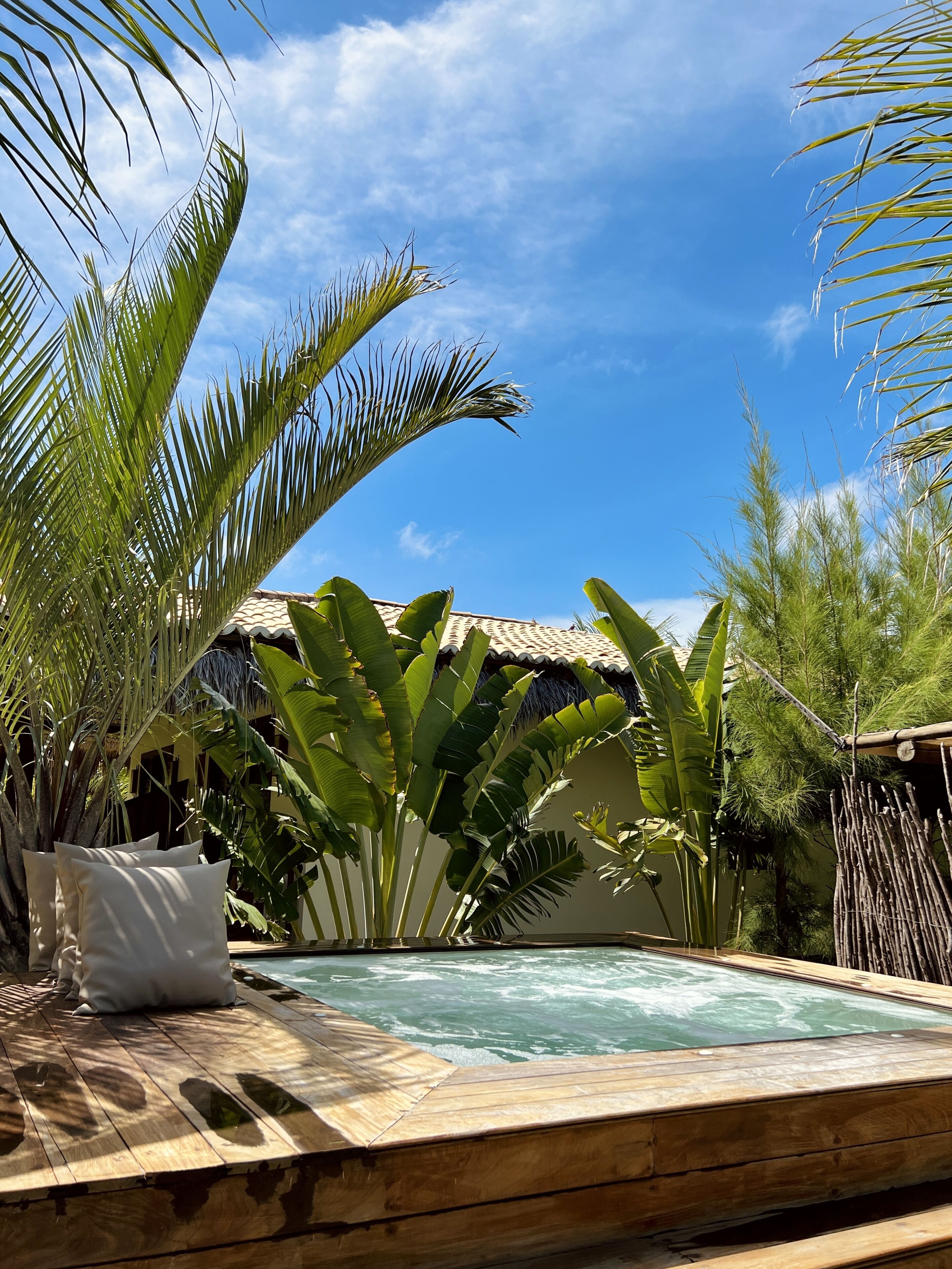 Une terrasse en bois avec une piscine, entourée de plantes tropicales et d’une structure à toit de chaume.