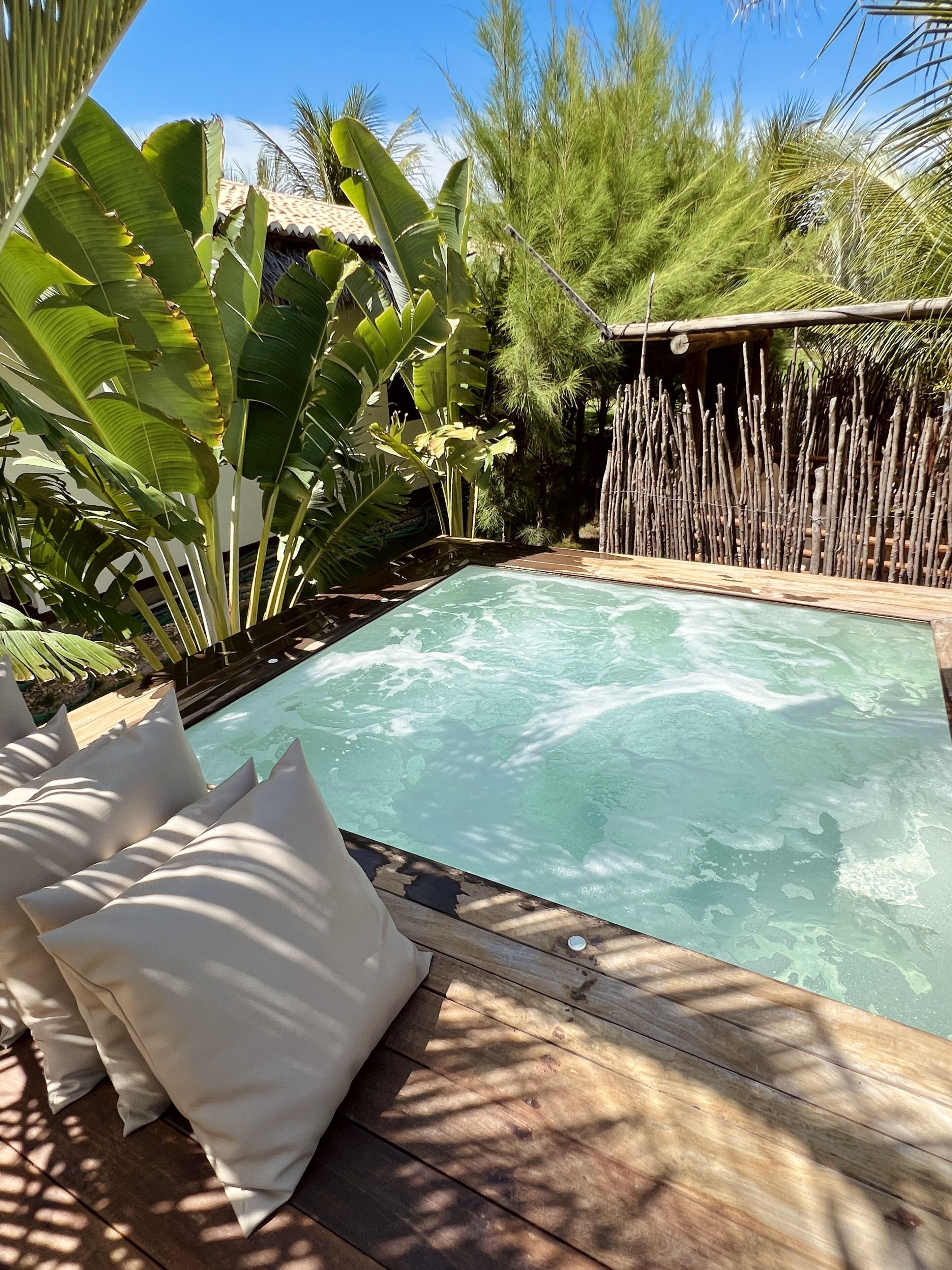 A rectangular pool with clear water, surrounded by wooden deck and white cushions.