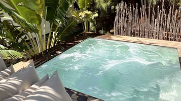 A rectangular pool with clear water, surrounded by wooden deck and white cushions.