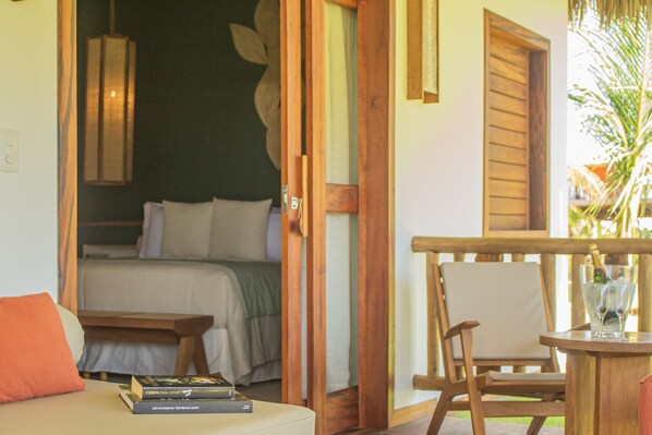 A room with a bed, a wooden chair, a small table with a glass, and a bookshelf with books.