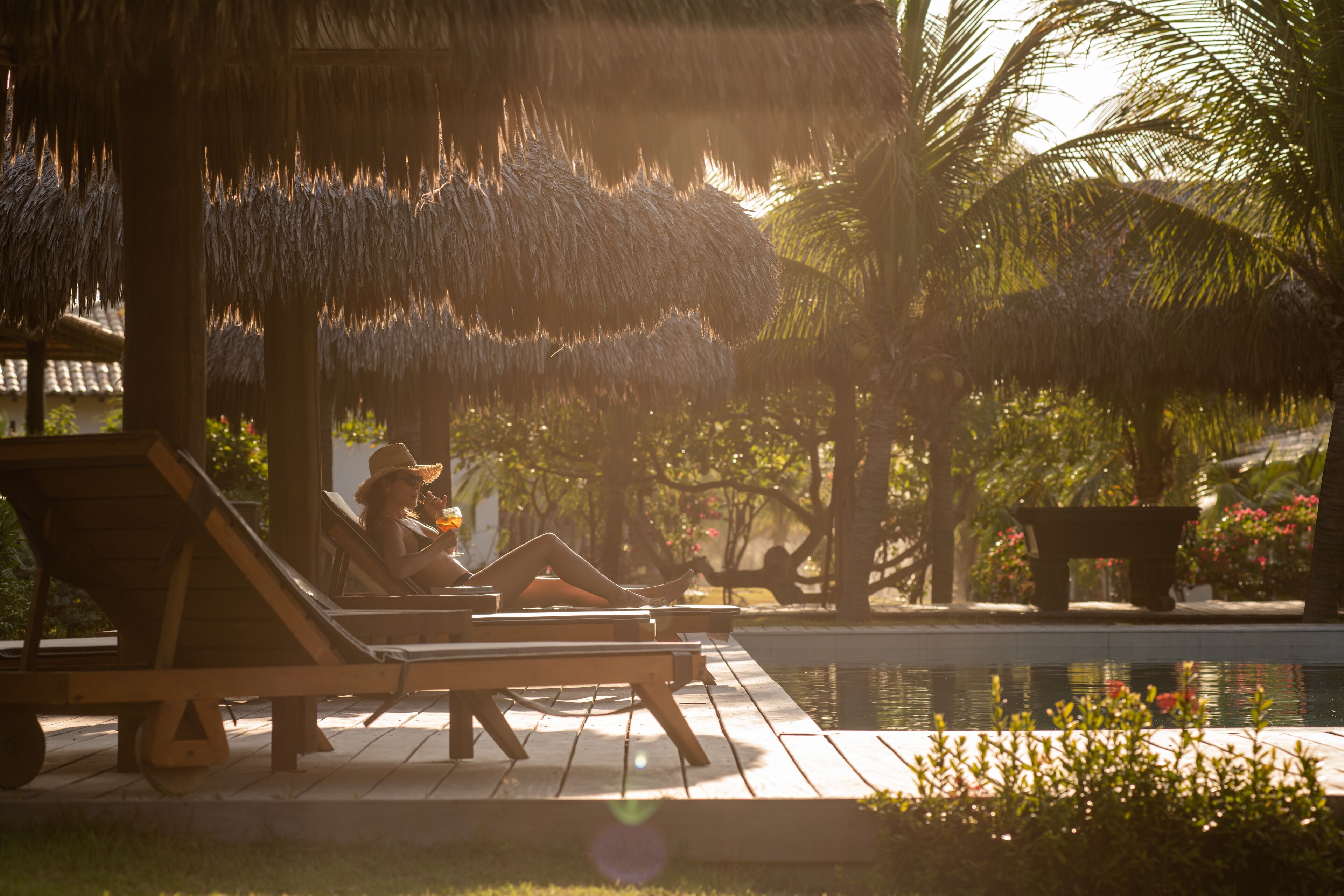 A poolside area with lounge chairs, a thatched roof structure, and a palm tree.