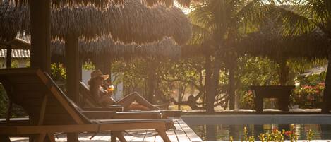 A poolside area with lounge chairs, a thatched roof structure, and a palm tree.