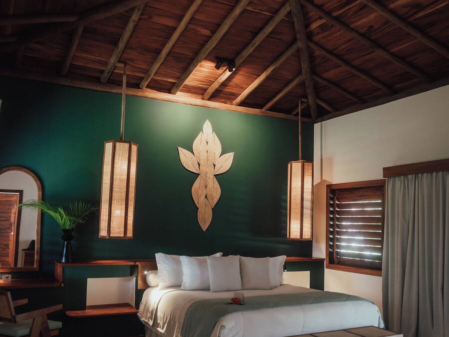 Ein Schlafzimmer mit Holzboden, einem Bett mit weißer Bettwäsche, einer Bank, einer Wandleuchte und einem Fenster mit Jalousien.