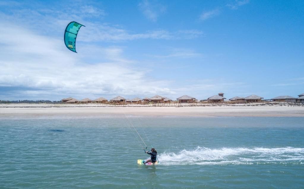 Una persona practica windsurf en una playa con cielo despejado.