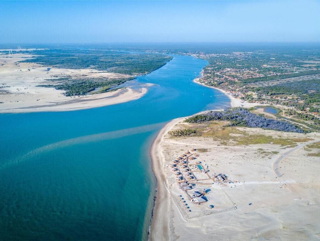 An aerial view of a coastal area with a large body of water, a sandy beach, and a small cluster of buildings.