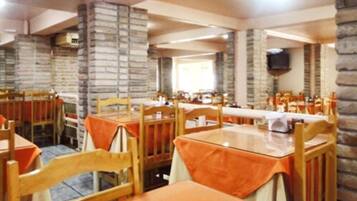 Un restaurant avec des tables et des chaises en bois, des murs en pierre et un téléviseur fixé au mur.