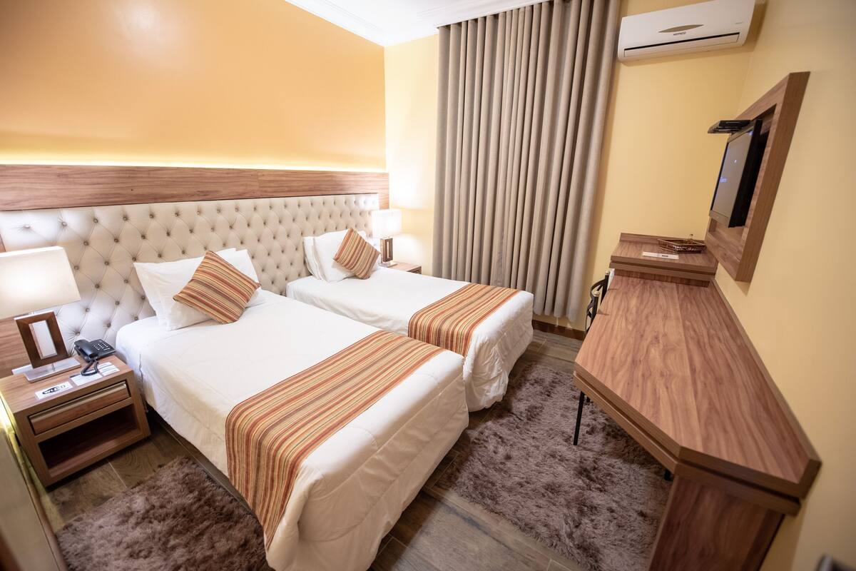 A hotel room with two beds, a wooden nightstand with a phone, a desk, and a TV.