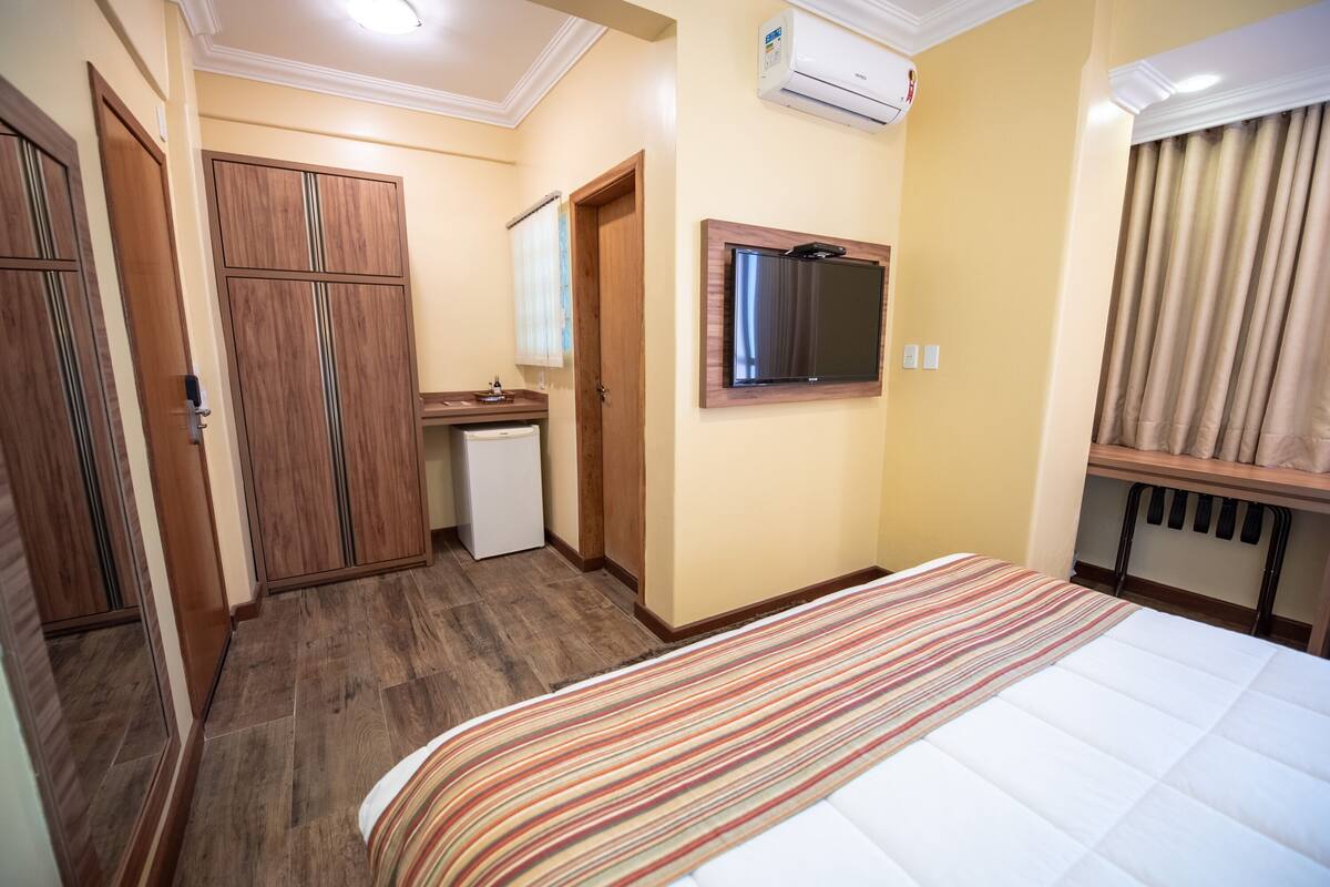 A bedroom with a bed, a small desk, a wardrobe, and a television.