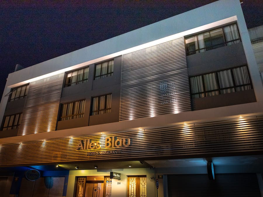 Fachada moderna de hotel con listones horizontales y señalización iluminada que dice "Altes Blau Hotel & Restaurant".