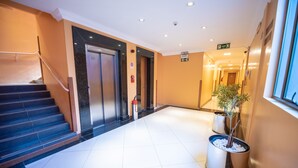 A hotel lobby with a staircase, elevators, and potted plants. - Hotel Alles Blau (Pelotas)
