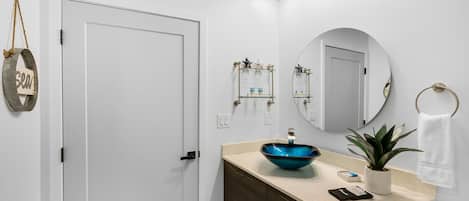 A modern bathroom with a white door, a blue glass sink, a mirror, and a small potted plant.