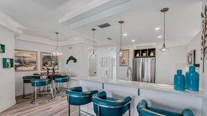 A modern kitchen with a central island, bar stools, pendant lights, and a refrigerator.