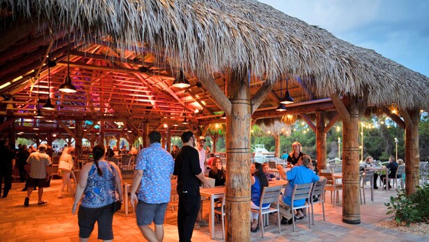 An outdoor dining area with thatched roof structures and wooden pillars.