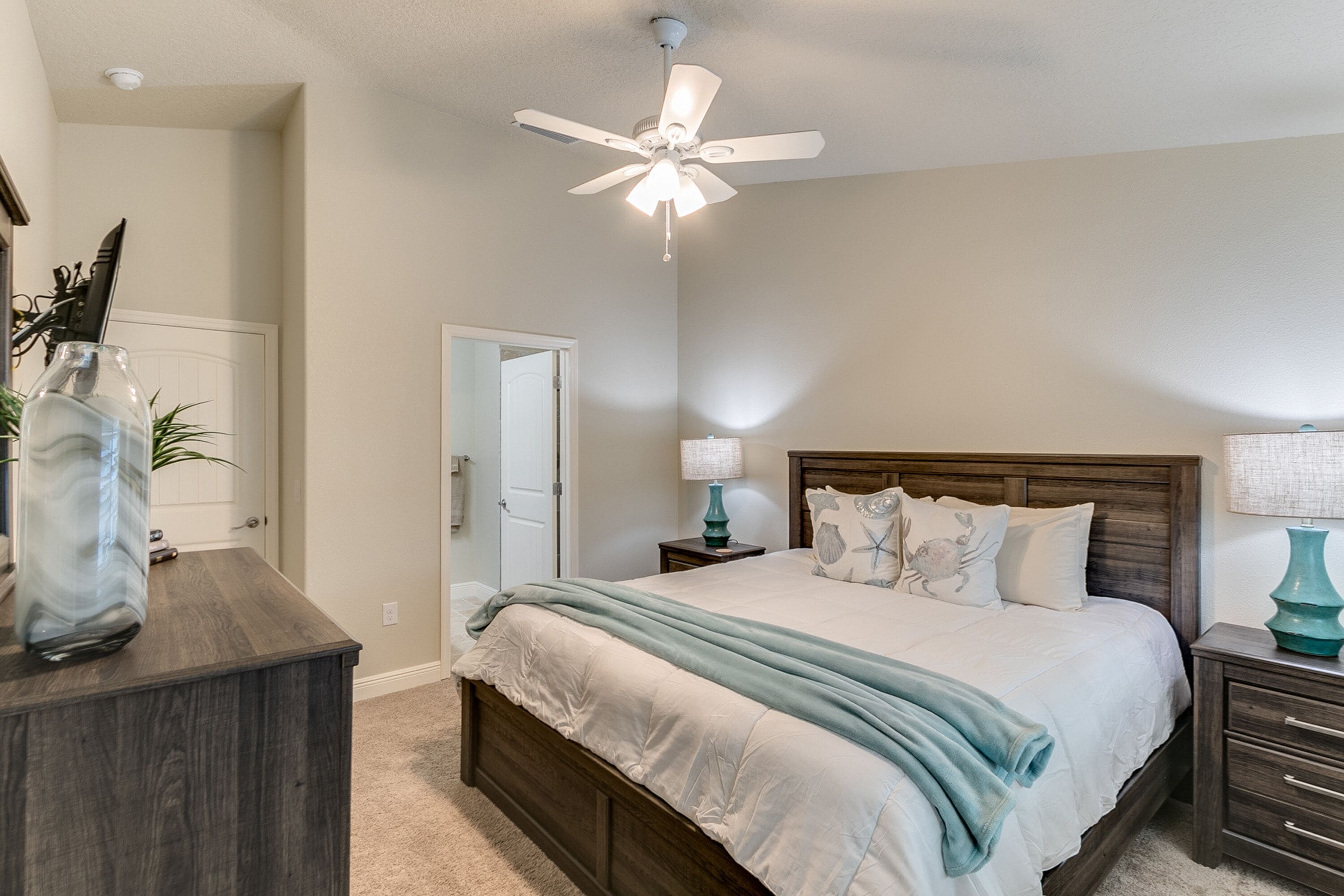 A bedroom with a bed, a nightstand, a dresser, a ceiling fan, and a door.