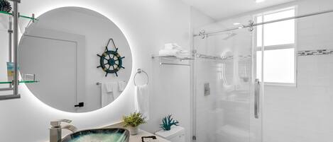 A modern bathroom with a glass-enclosed shower, a round mirror, and a vessel sink.