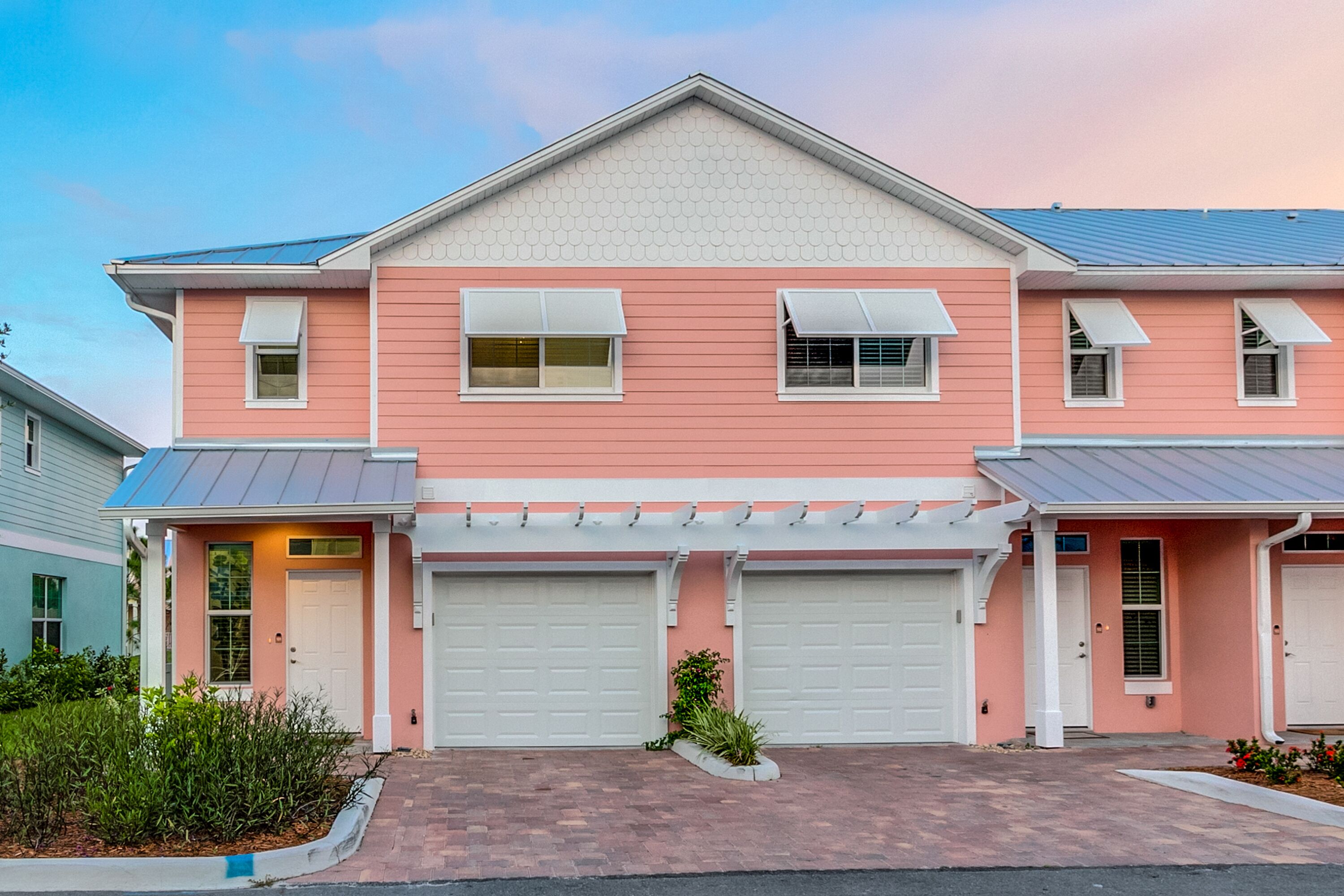 Una casa a due piani con facciata rosa, portoni del garage bianchi e un portico anteriore coperto.