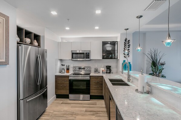 A modern kitchen with stainless steel appliances, a marble countertop, and pendant lighting.